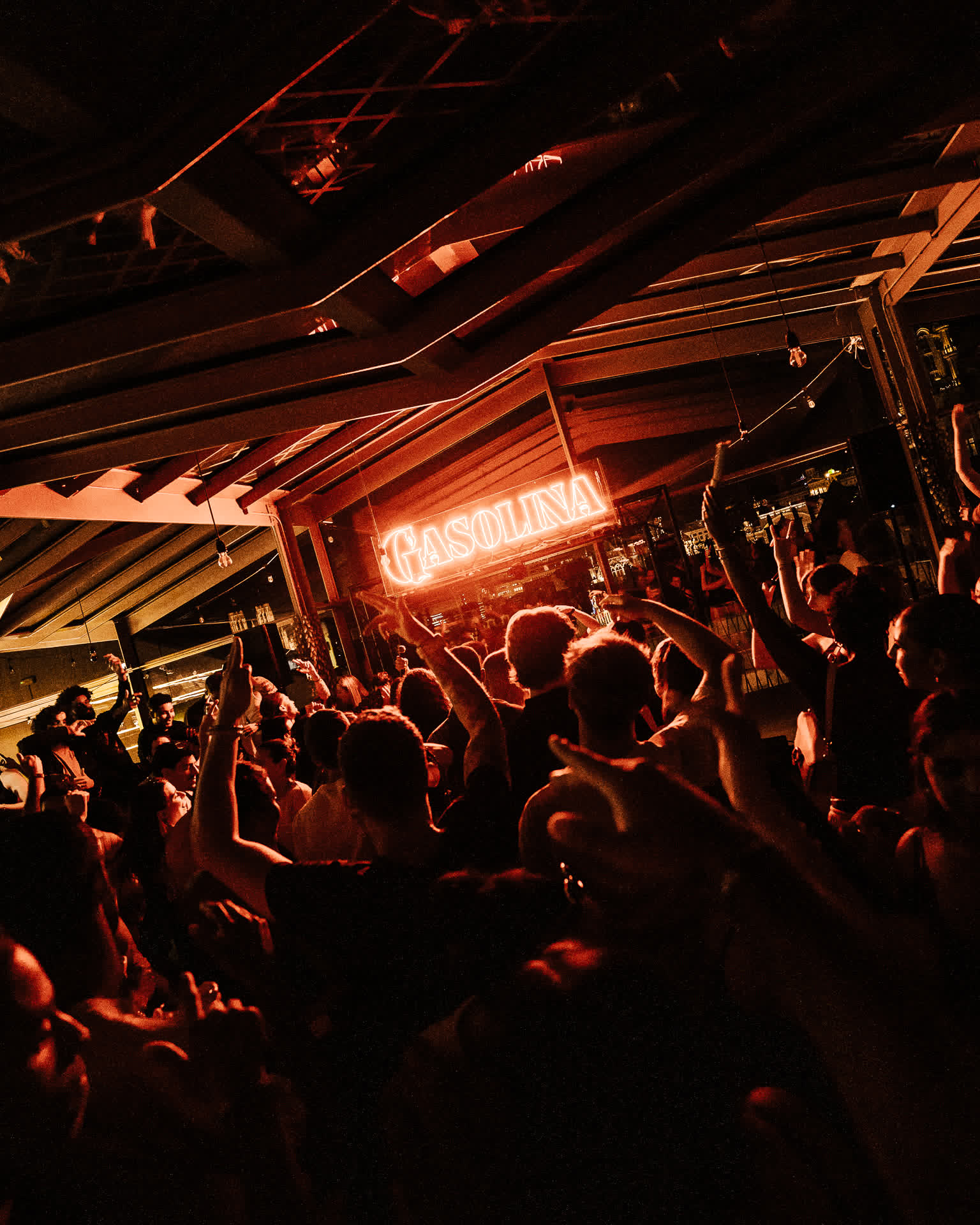 Hands raised under the Gasolina sign in warm amber light